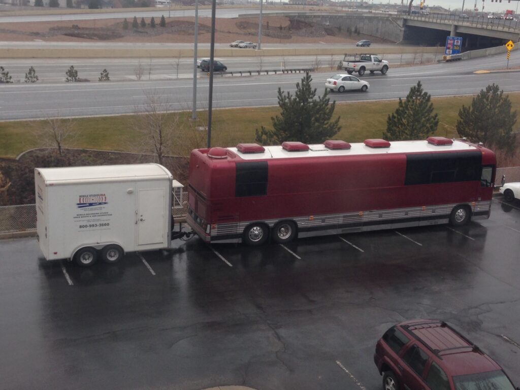 The "Mobile Studio USA" trailer is seen attached to a large maroon tour bus belonging to the band Pentatonix, parked in a lot. The trailer setup indicates it&rsquo;s ready to support audio recording needs on the road.