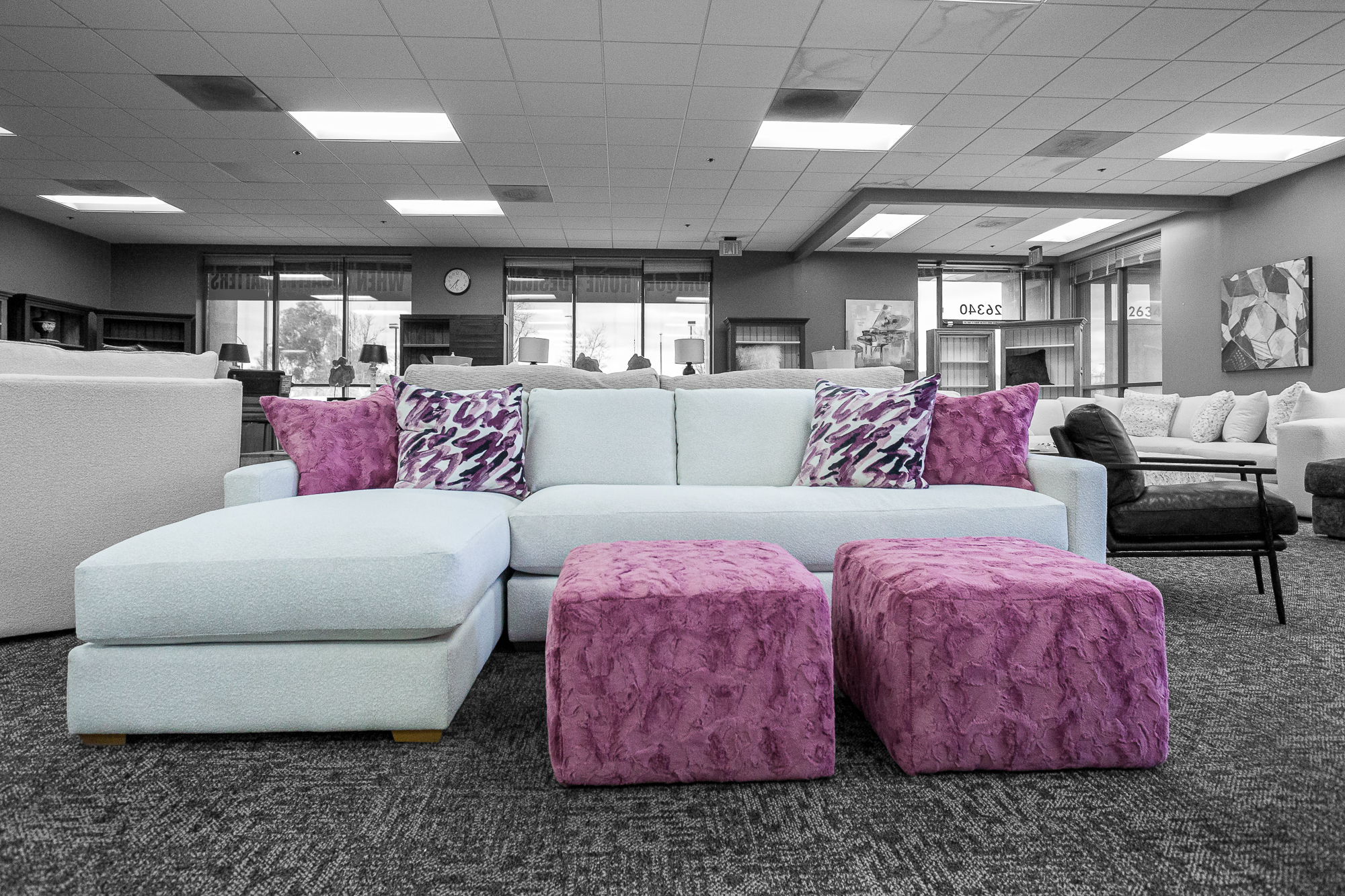 A large white Angel Cloud sofa chaise with two faux-fur square purple ottomans in front. Matching purple and patterned accent pillows are on both sides of the sofa.