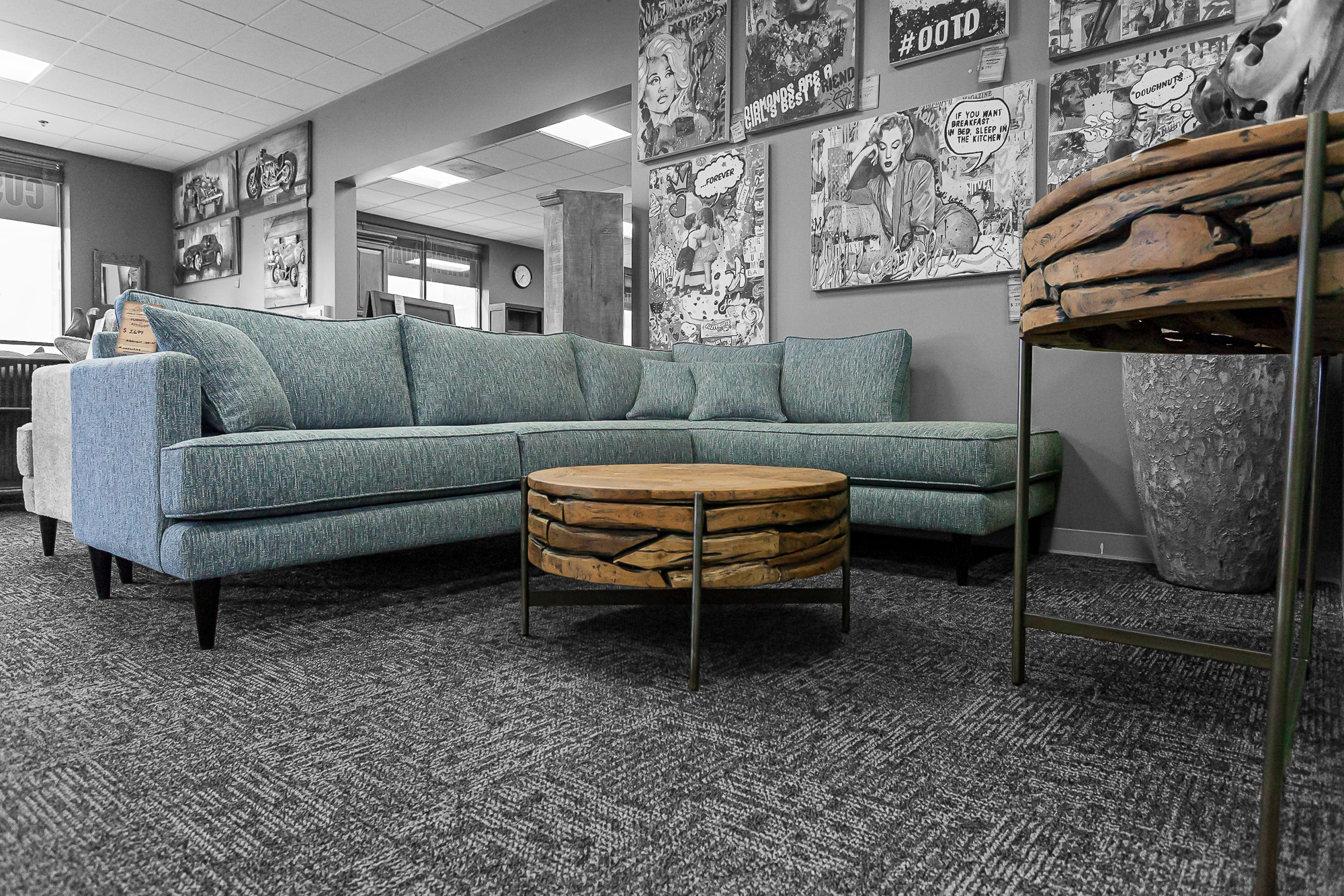 A teal sectional paired with a sculptural round wood coffee table, set in front of comic art gallery walls.