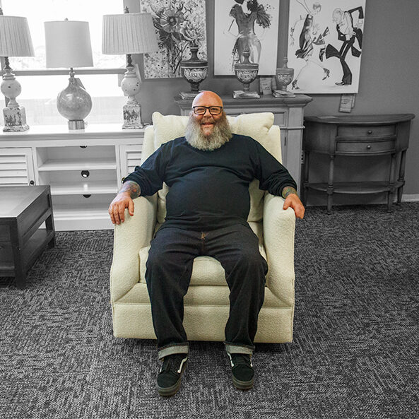 Owner of Furniture with Attitude, Tony Peyser, sitting in one of his custom made chairs in front of store merchandise.