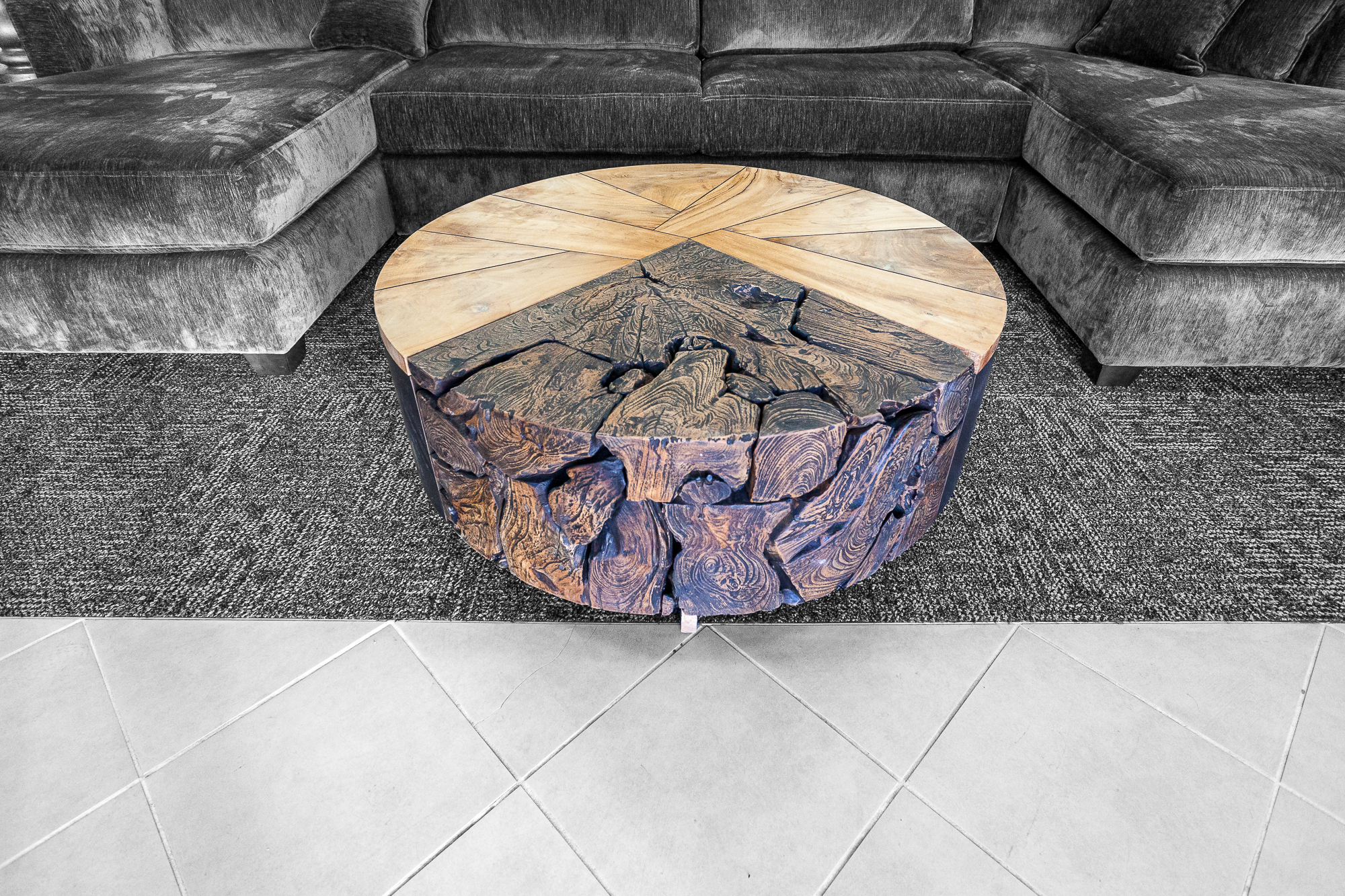 A circular wood-inlay coffee table in front of a deep charcoal sectional.
