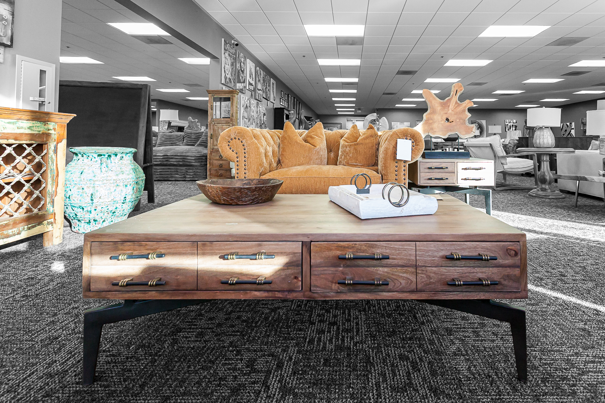 Large wood coffee table with drawer pulls, placed in front of a golden velvet couch with artisan decor accents behind.