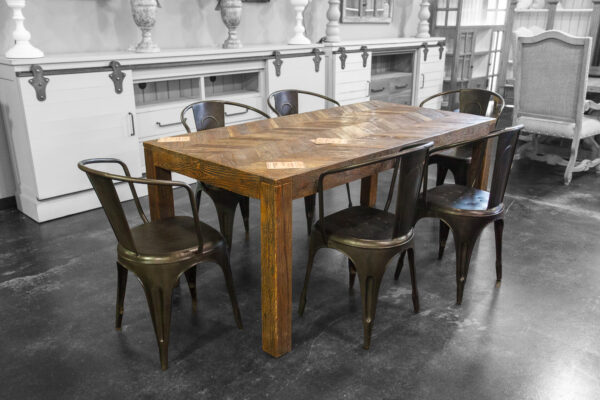 Rectangular solid wood dining table with a chevron pattern top, surrounded by six black industrial-style metal chairs.