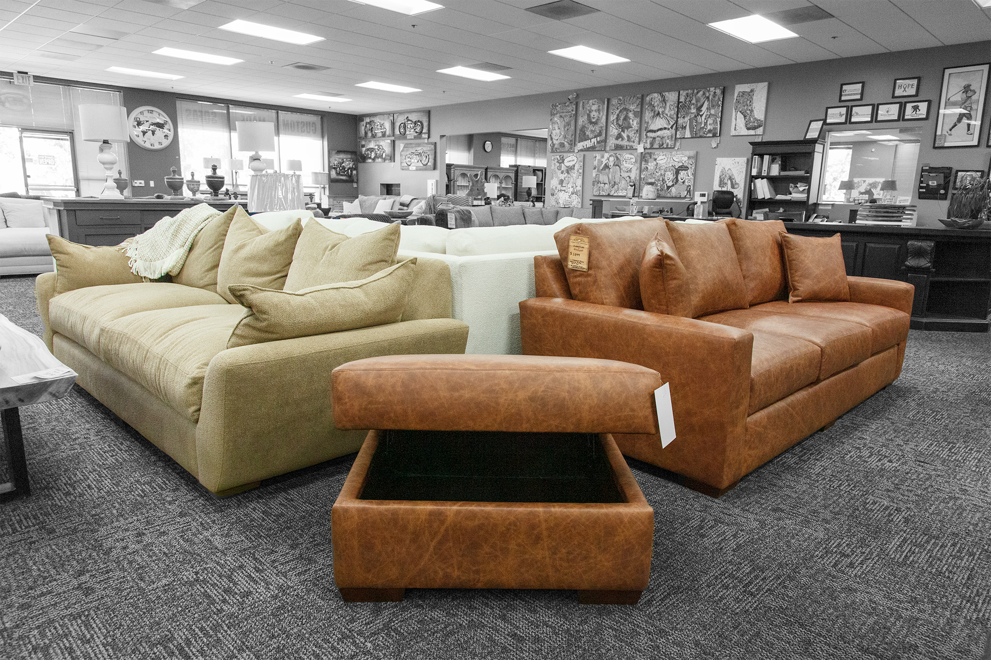 Tan velvet sofa with oversized pillows next to a brown leather sofa and a matching lift-top storage ottoman, displayed in a spacious showroom.
