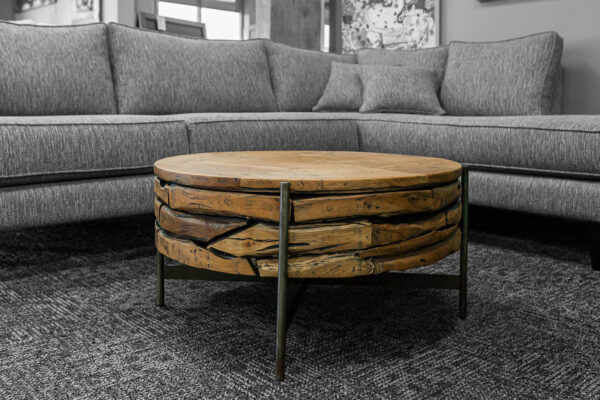 Round reclaimed wood coffee table with stacked, textured layers and black metal legs, placed in front of a gray upholstered sectional.
