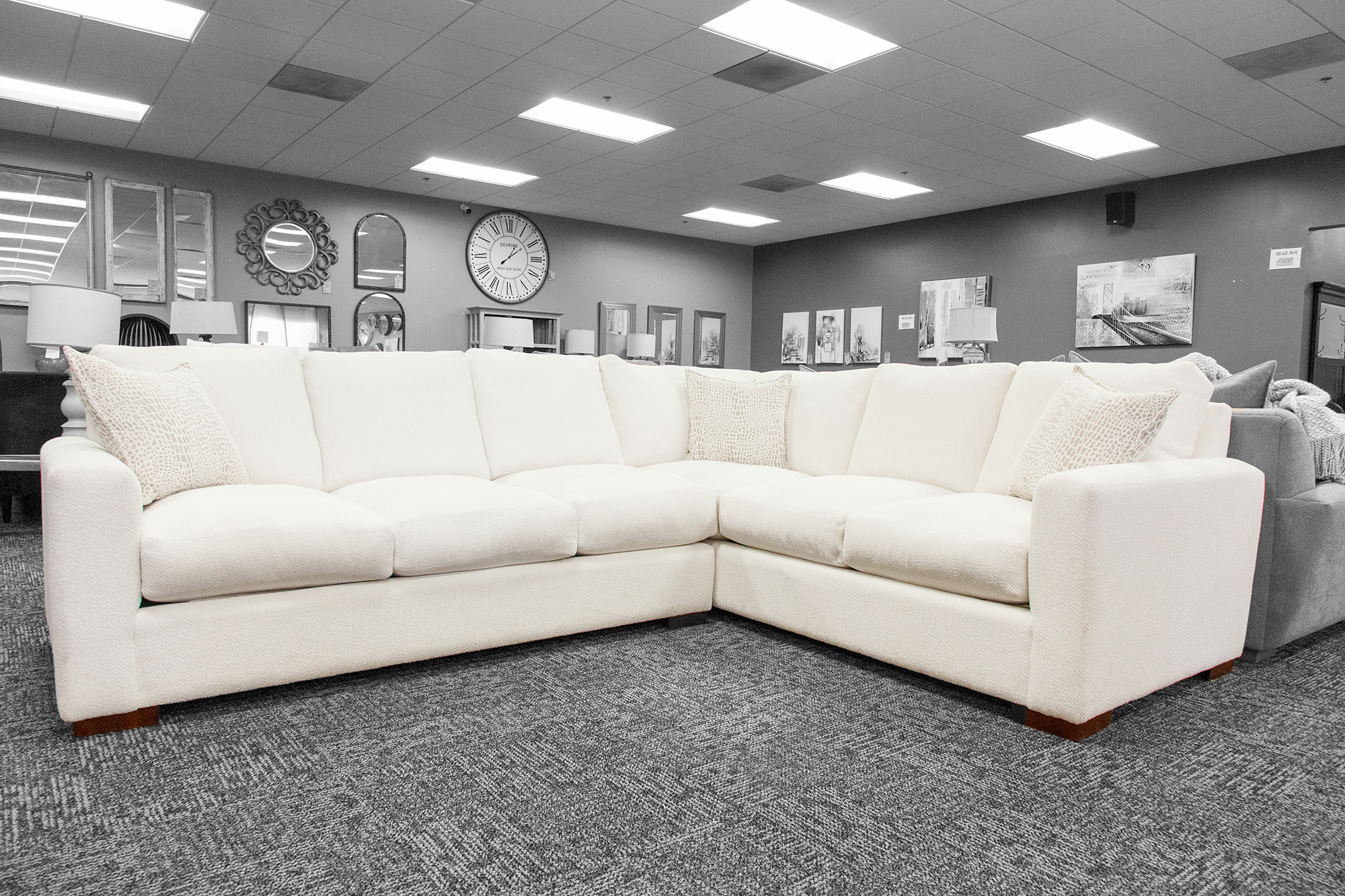 Clean-lined ivory sectional sofa with neutral pillows, set against a gallery wall of round mirrors and wall art.