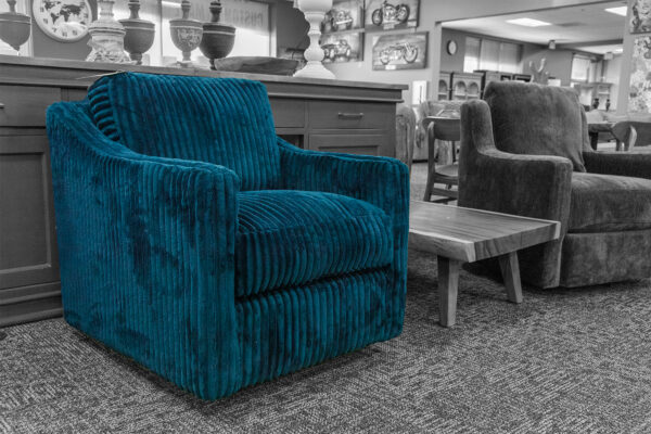 Teal corduroy swivel chair in a showroom with solid wood furniture in the background. The bold texture and color contrast with a neutral-toned interior.