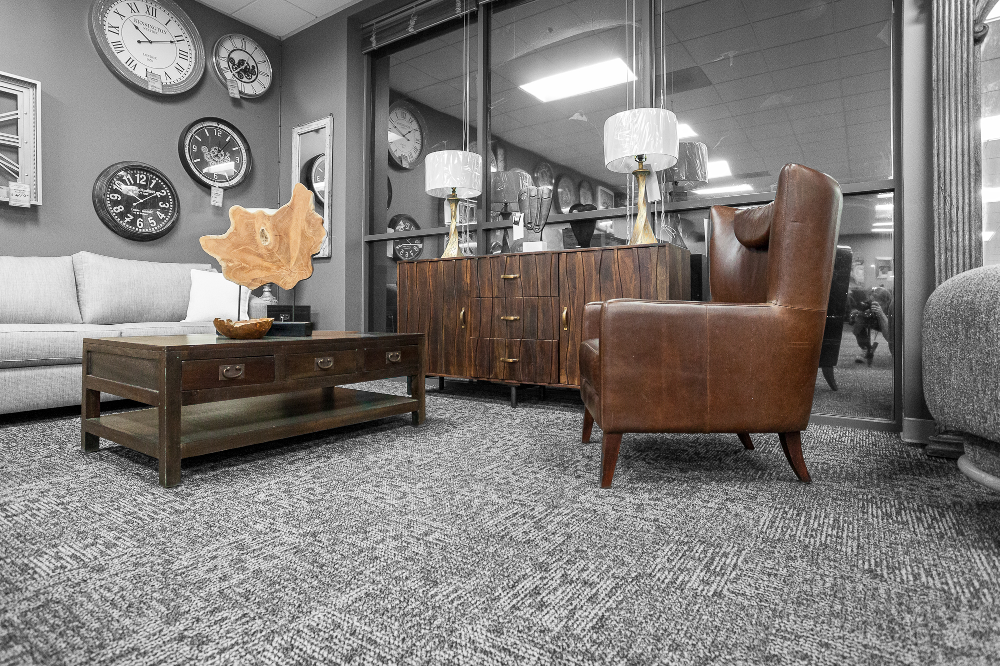 A brown leather wingback chair with a live-edge sculpture on a dark coffee table, beside a carved wood cabinet.