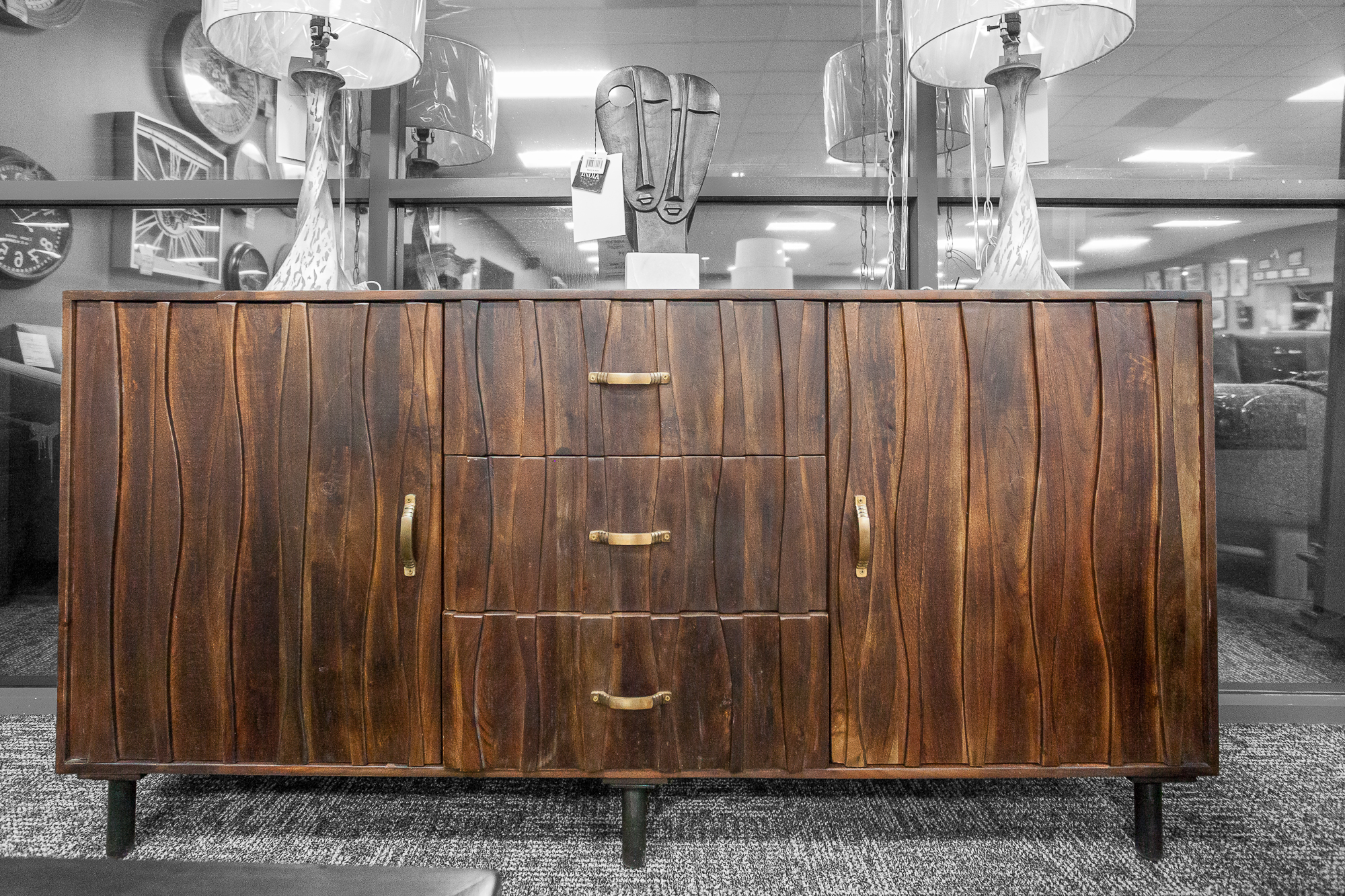 A mid-century modern sideboard made from solid wood and an ornate wave pattern front. It has three drawers and two side storage. 