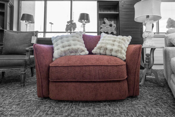 Wide red armchair with soft textured fabric and two white faux fur pillows, centered under a large showroom window.