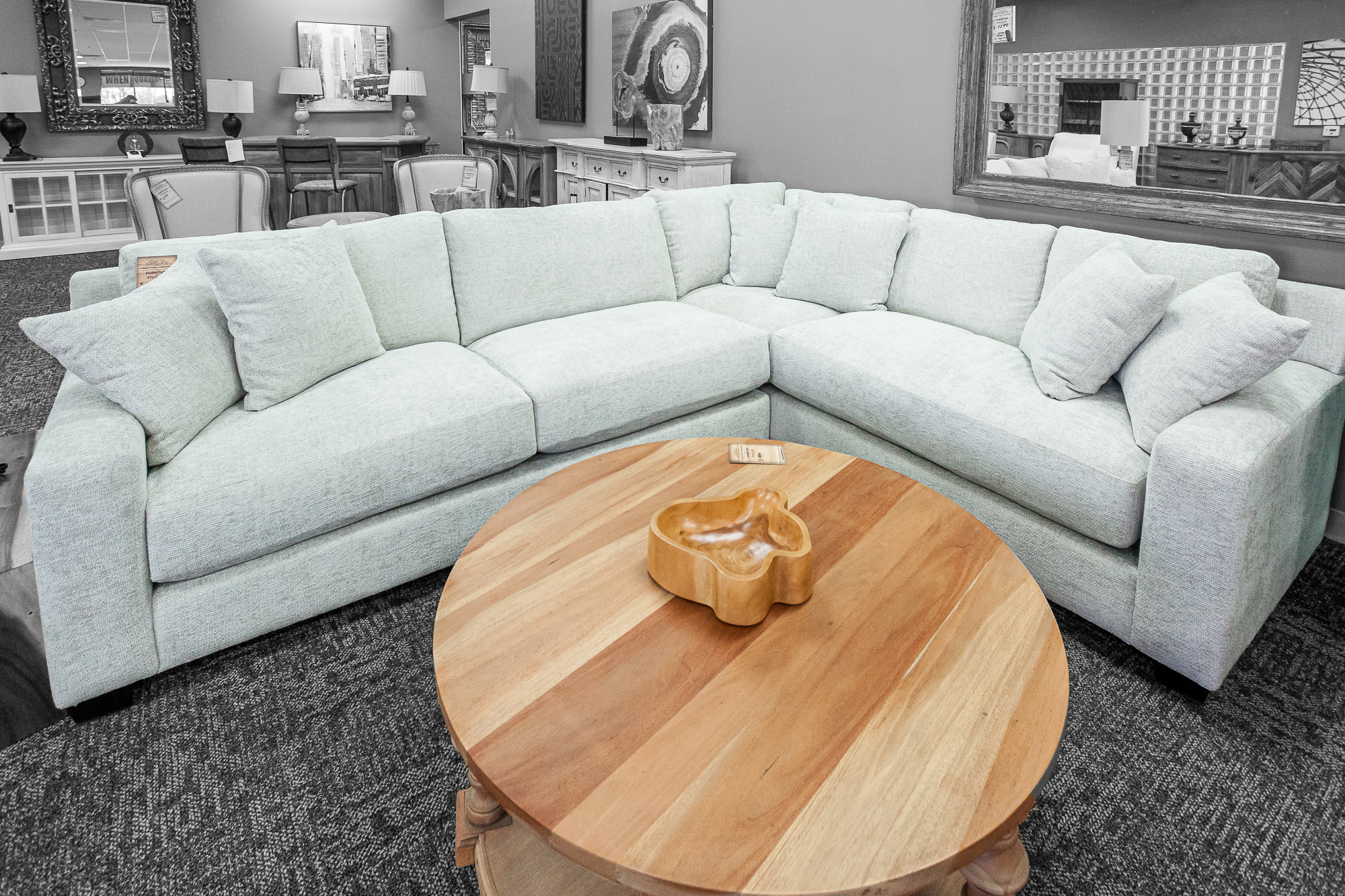 A white sectional sofa wrapped around a circular wood coffee table with angled slats.