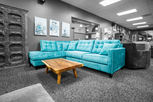 Large teal sectional sofa with tufted cushions, paired with a live edge wooden coffee table and surrounded by wall art.