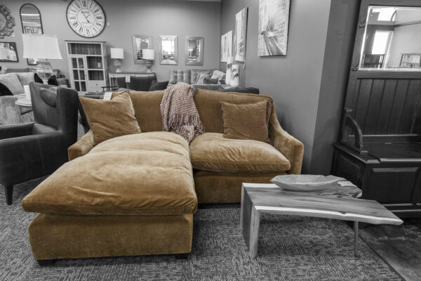 Low-profile mustard yellow-brown chaise sectional with overstuffed cushions and a live edge wood side table in a cozy showroom corner.