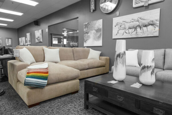 Beige sectional sofa with rainbow fabric swatches draped on the chaise lounge, displayed in a furniture showroom with neutral d&eacute;cor.
