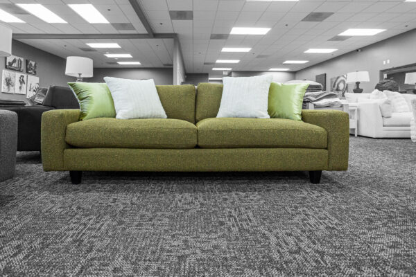 Green upholstered sofa with clean lines and white and light green pillows, placed in the center of a well-lit showroom.