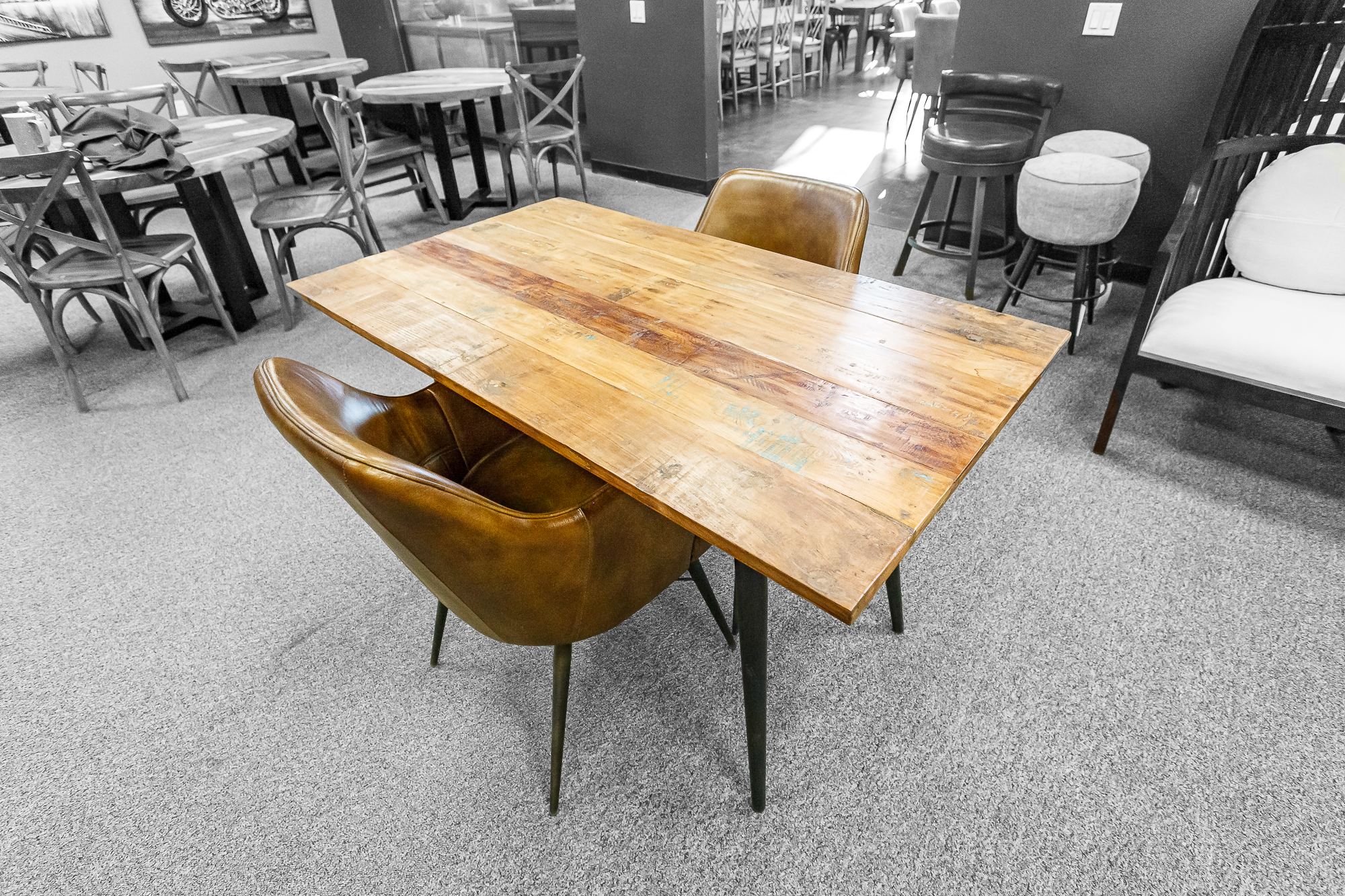 A small reclaimed wood table paired with two smooth brown leather chairs in a cozy showroom corner.