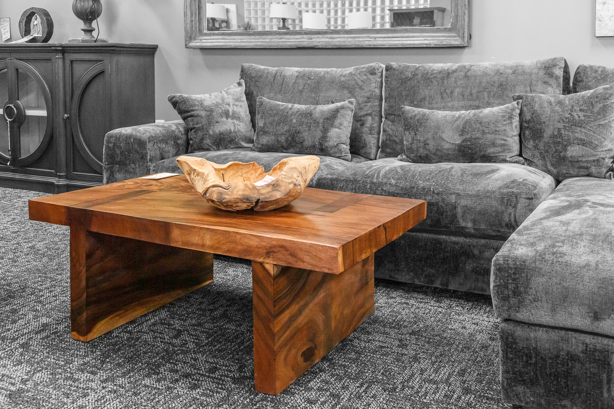 A square walnut coffee table with live edge-style base paired with a plush grey sectional.