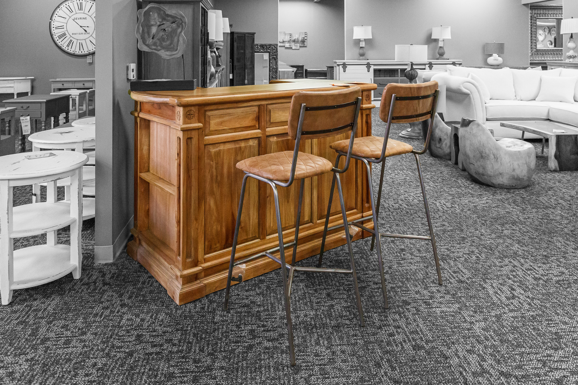 Natural wood home bar cabinet with black metal stools, set against matching console furniture.