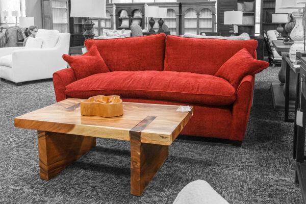 Red loveseat with plush cushions in a showroom, styled with a live-edge solid wood coffee table with metal inlays.