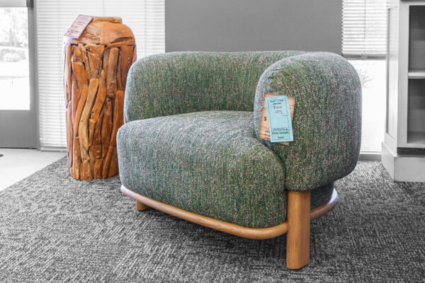Curved accent chair with speckled green upholstery and a wood frame, styled beside a raw wood pedestal side table in a bright entry space.